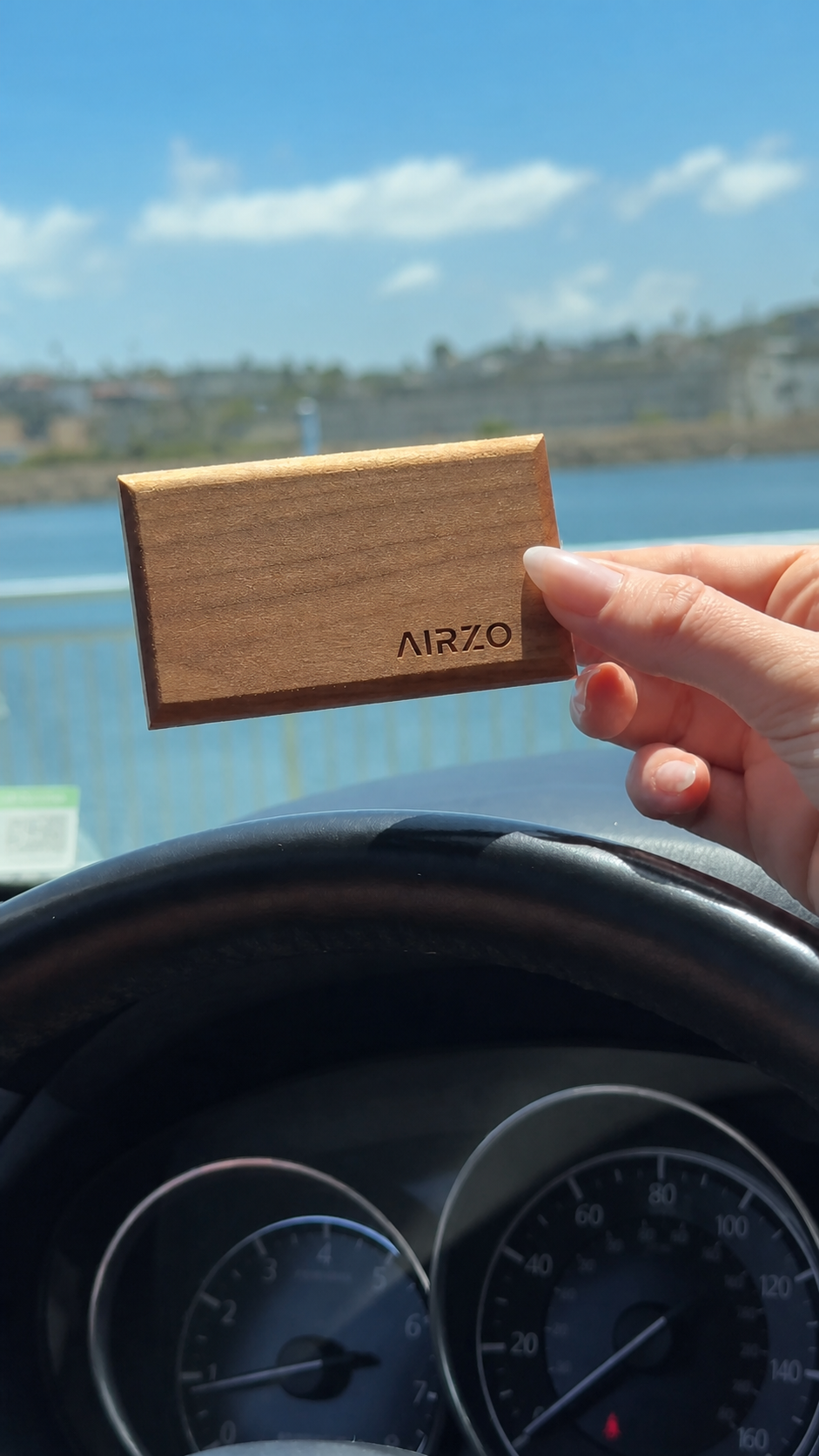 The AIRZO Wood Car Freshener held in hand, showing the scented wooden block and magnetic metal visor holder